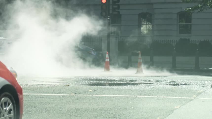 Cars and a truck driving down a city street emitting smoke