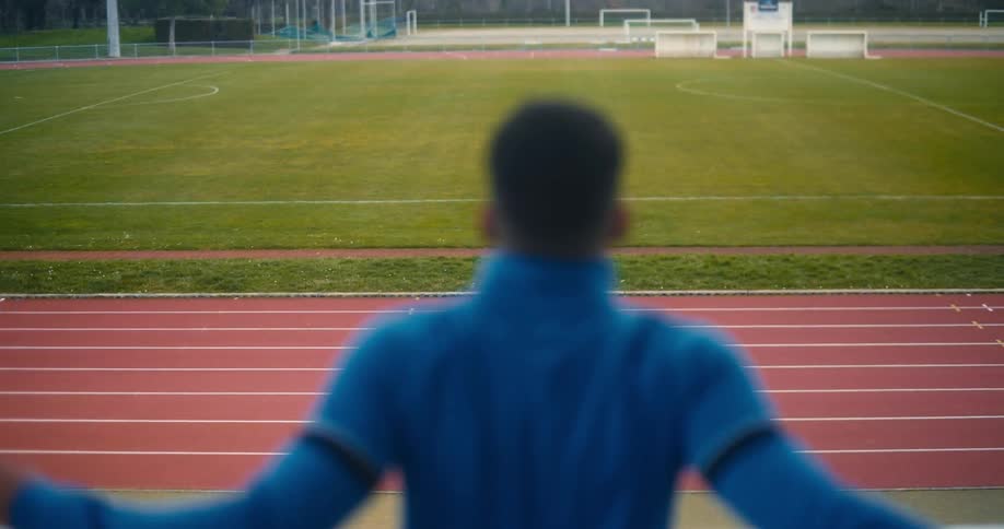 Man standing in front of a running track stretching his arms