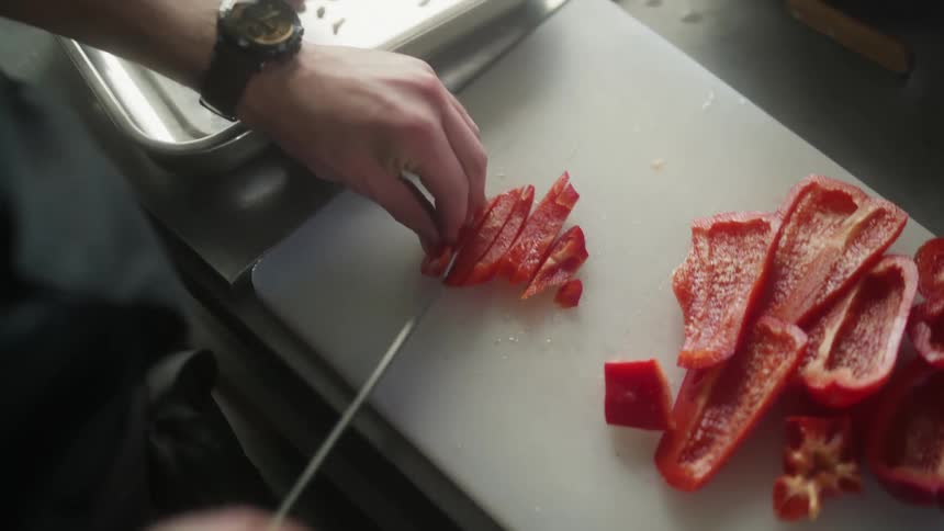 Hands with a knife cutting red pepper