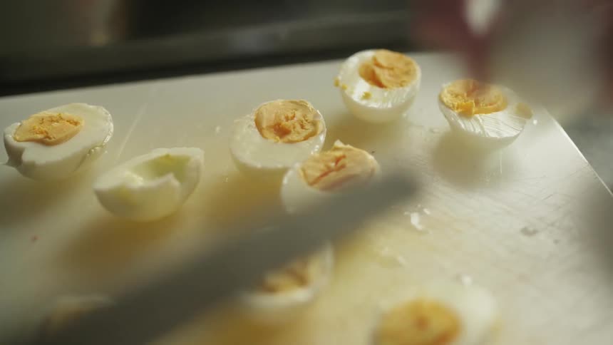 A person cutting a boiled egg in half with a knife on a cutting board