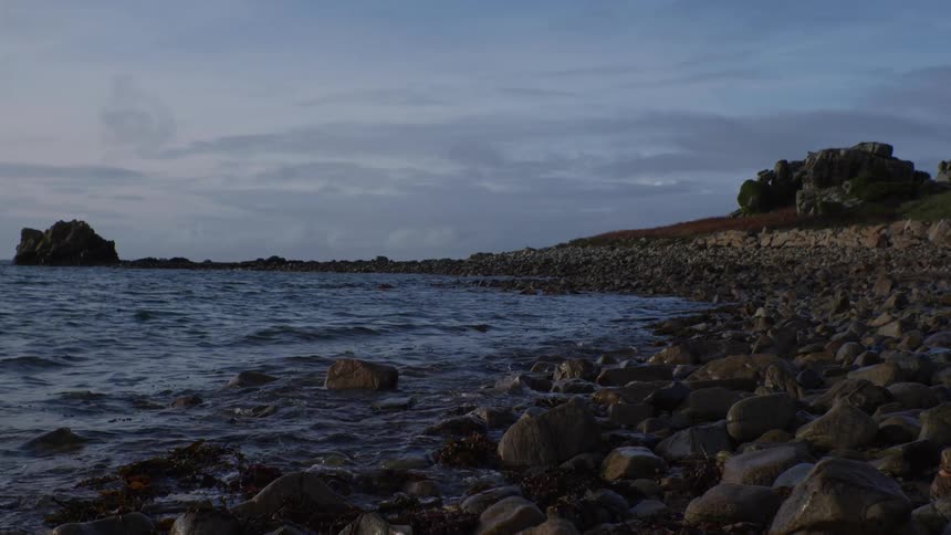 Calm sea with waters reaching rocks and stones on a morning with a purple sky