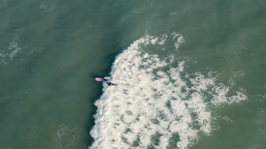 Aerial view of two people surfing wave in ocean