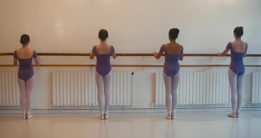 Four young female ballerinas in matching outfits practice moves in a studio