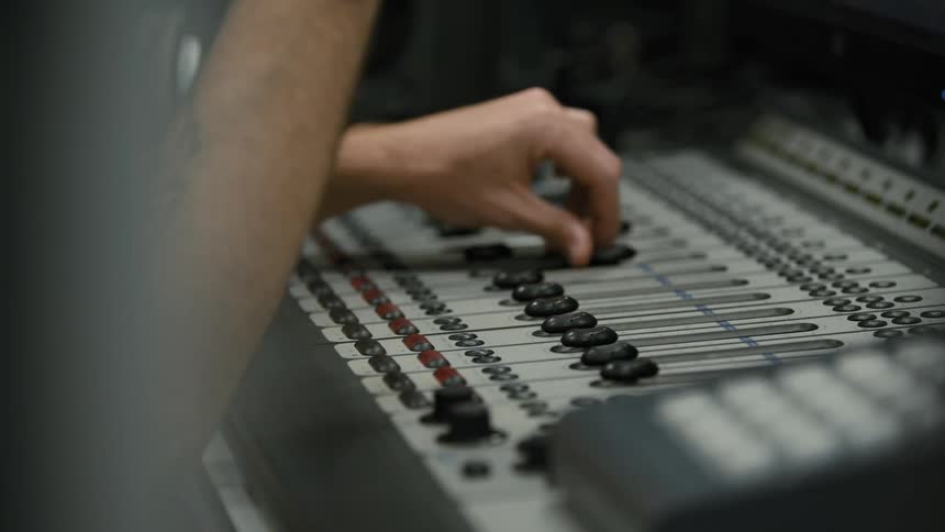 Extended arm adjusting audio levels on a mixing board
