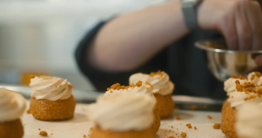 Hands pouring crumbled cookie pieces onto cupcakes with white frosting