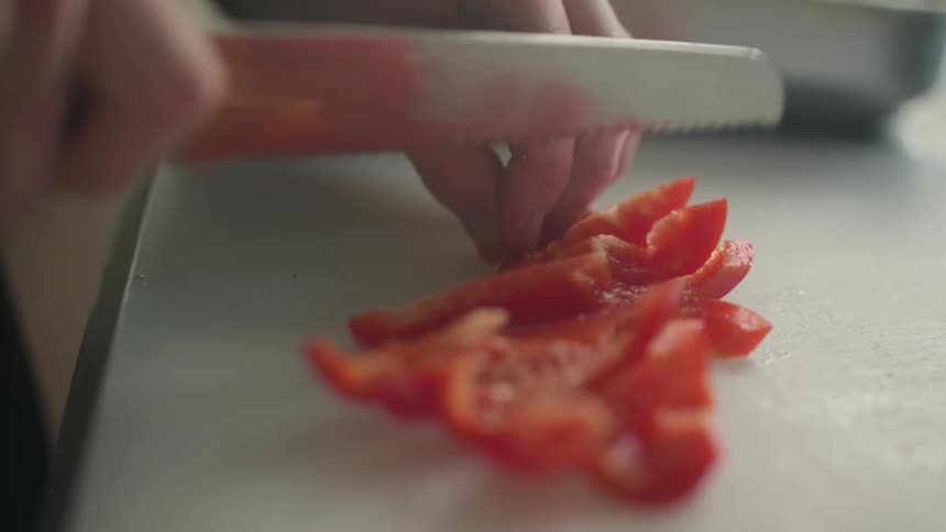 A person dices up a red pepper on a white cutting board