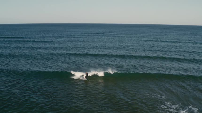 Aerial view of a person alone in the ocean surfing a wave