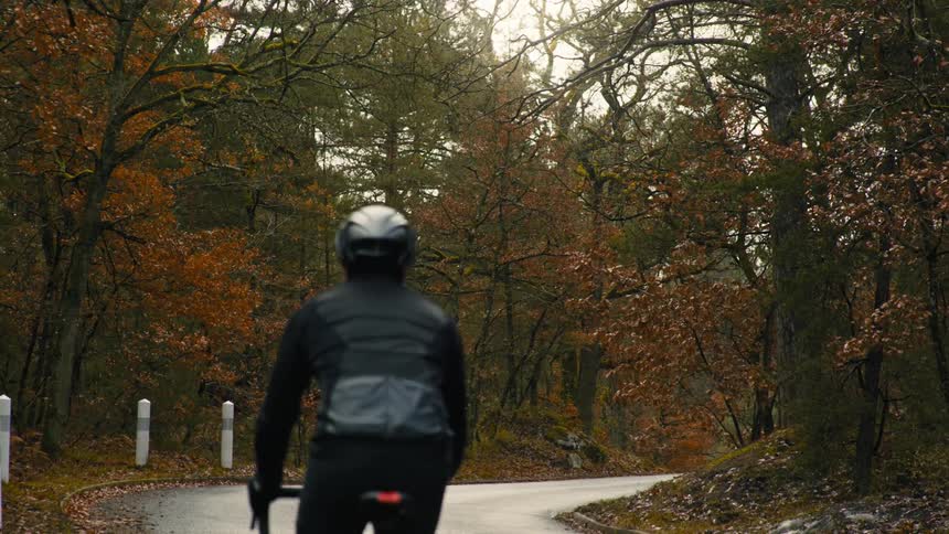 A cyclist wearing a black jacket and crash helmet rides on a road through the countryside