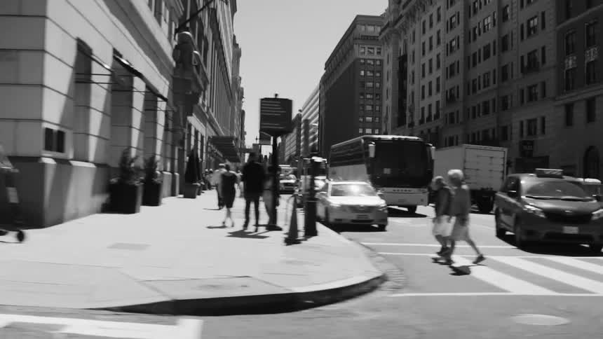 Black and white footage of a busy city street on a sunny day