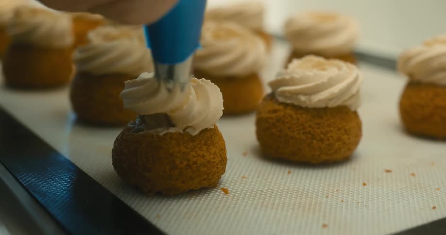 Close up of a hand piping cream onto a pastry