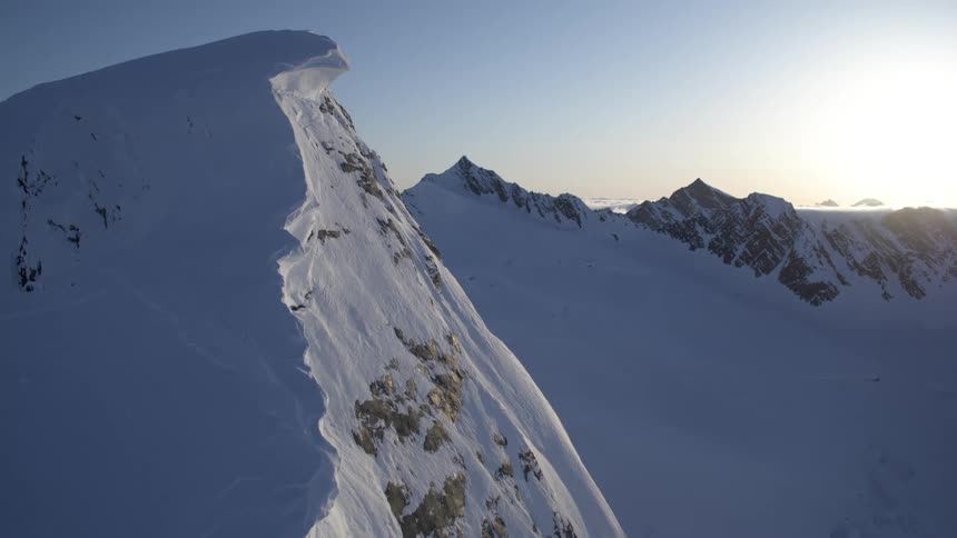 A snowcapped mountain ridge stretches towards the horizon bathed in the soft light of dawn