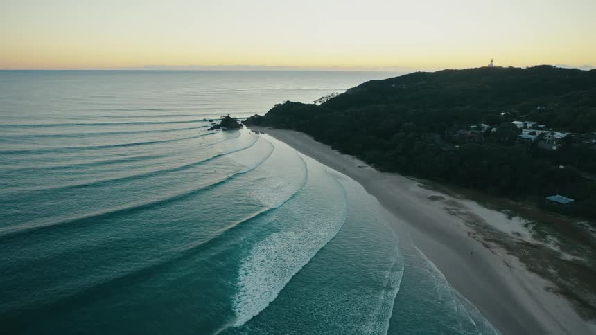 Waves roll onto the beach near a coastal town surrounded by forest