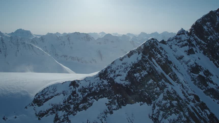 Rocks show through the snow on the tops of mountains at high noon