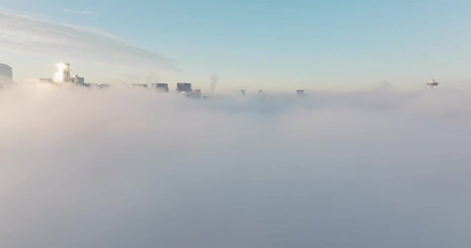 Ascending over a layer of fog to reveal the tops of tall buildings along the Seattle skyline