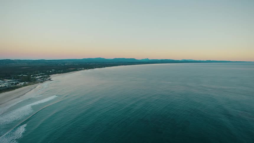 A coastline stretches into the distance with a beach and rolling waves in the foreground