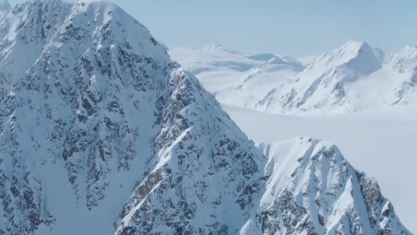 A snow capped mountain range stretches out into the distance its peaks glistening under a clear blue sky