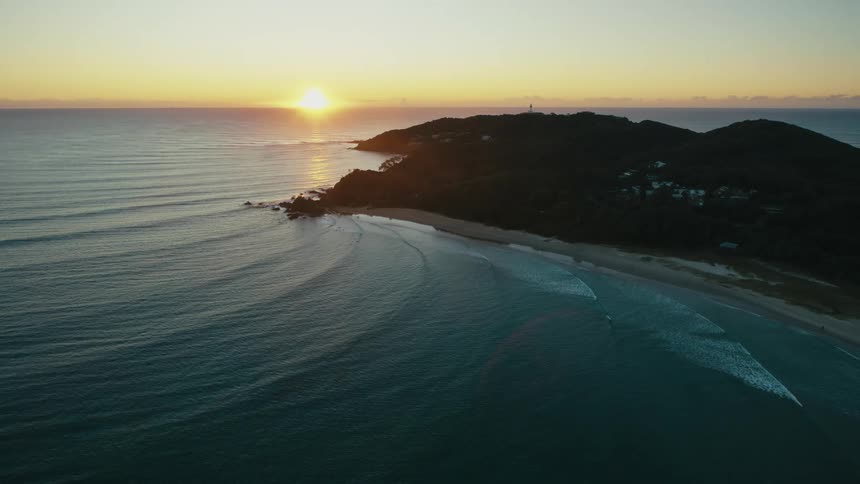 Aerial view of an island with a beach and the golden sun on the horizon