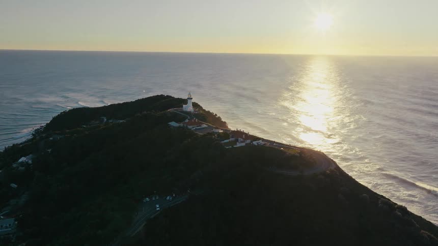 Aerial panorama of the last lighthouse and other buildings on the peak of a seaside crust and the sun on the horizon