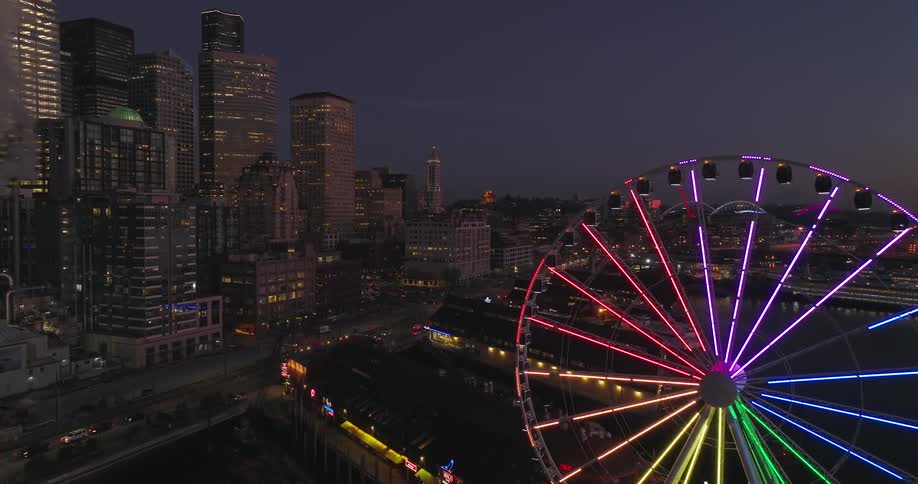 A colorful ferris wheel stands illuminated against the backdrop of the Seattle skyline