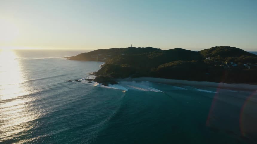 Aerial landscape of a beach with the sun rising on the horizon and the coast in the background