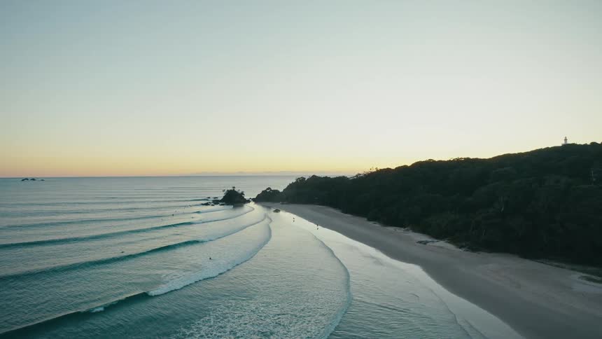 Large foamy waves crest on a beach as the sun shines on the horizon