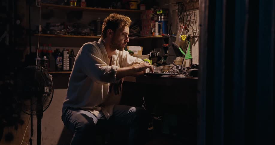 Concentrated man sitting inside a garage with tools
