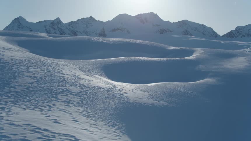 Panorama of layers of snow with mountains and the sun in the background