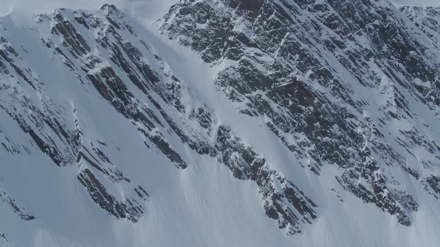 A rugged snow covered mountain slope with jagged rock formations partially visible beneath the snow