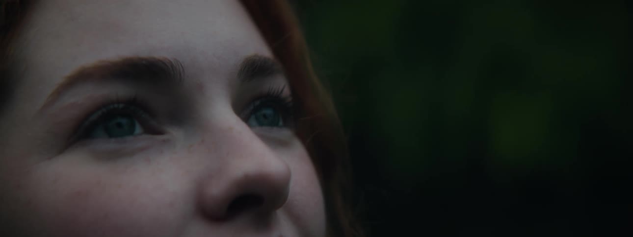 A teenage girl with red hair stares upwards with a smile on her face