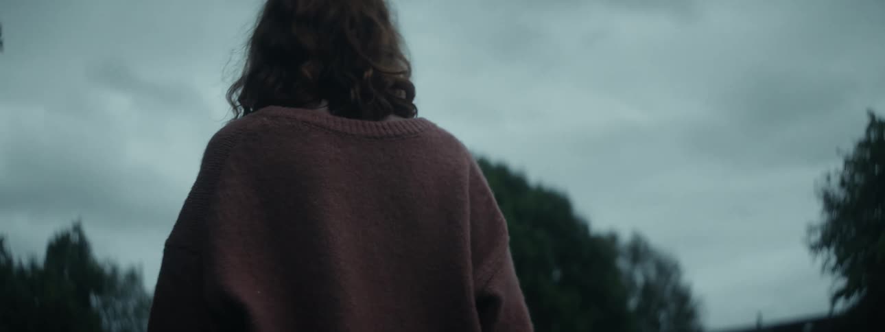 The back of a person with curly hair wearing a brown sweater walking outdoors