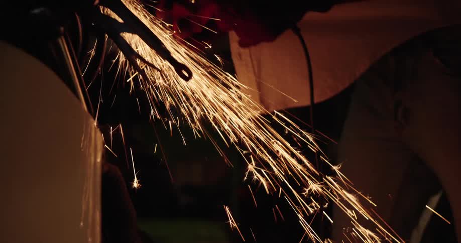 A person uses a grinding tool on a metal surface creating a shower of sparks