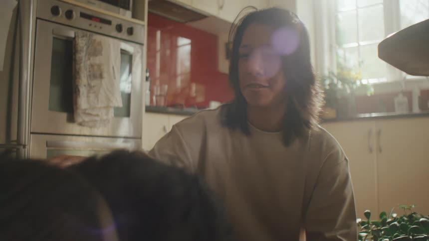 A young woman in a beige sweater leans over to pet a dark haired dog
