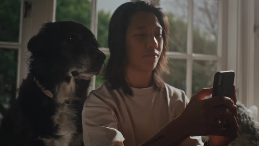 A person holding a smartphone while sitting next to a black and white dog