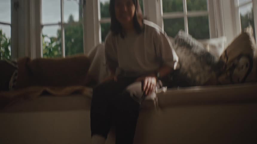 Dog runs up to woman sitting on the couch in the living room