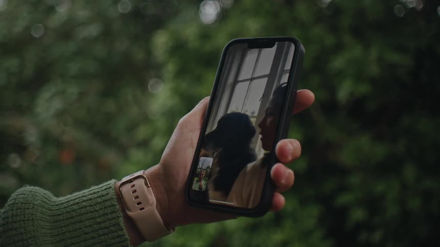 Close up of a persons hand holding a smartphone talking to a woman and a dog