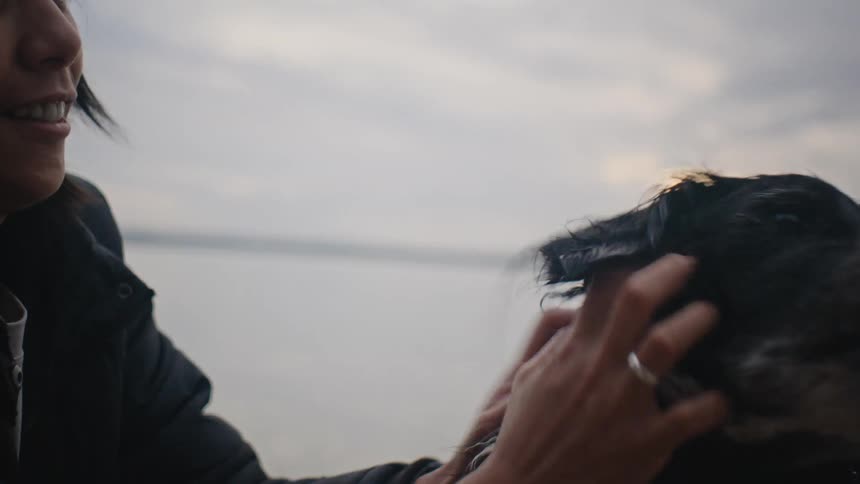 A woman pets her black dog and smiles as it looks up at her