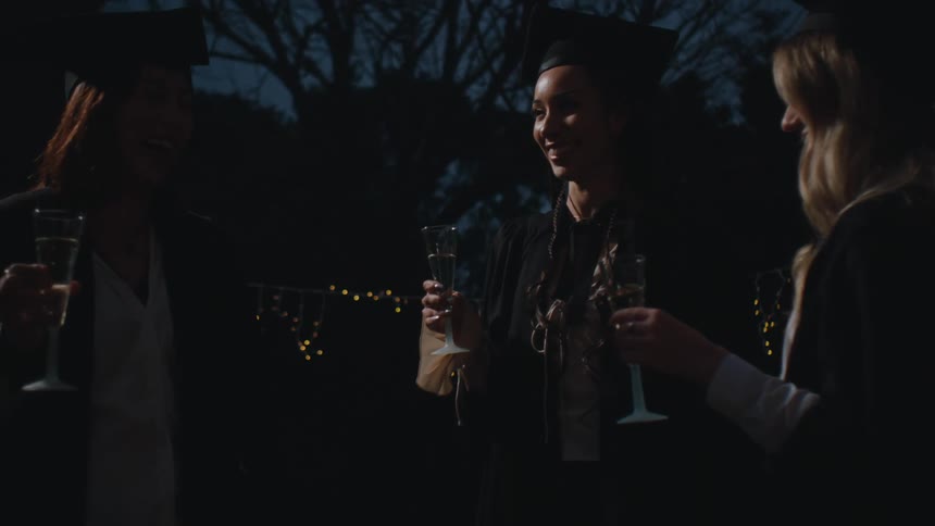 Three women in graduation gowns toasting glasses of champagne