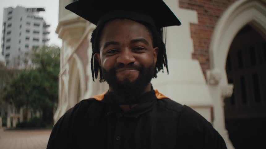 Black man smiling in excitement for the camera in his cap and gown