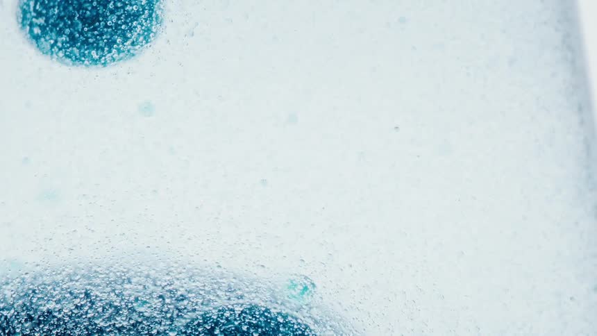 Several blue spheres covered in tiny bubbles float in a clear liquid