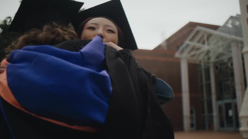 Two female graduates with gowns hugging each other