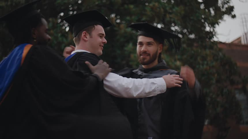 Students hugging each other while all wearing graduation gowns