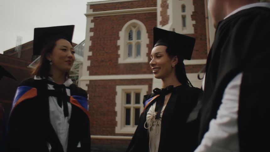 A group of graduates wearing caps and academic robe has a conversation