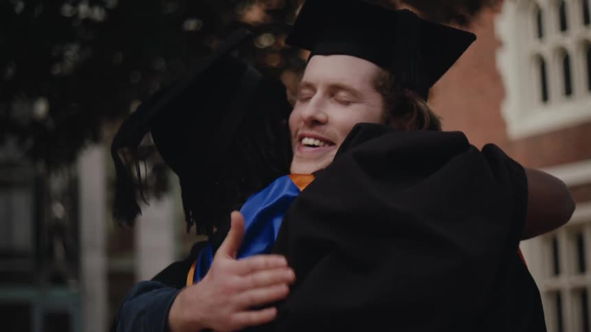 Two students hugging each other while wearing graduation gowns
