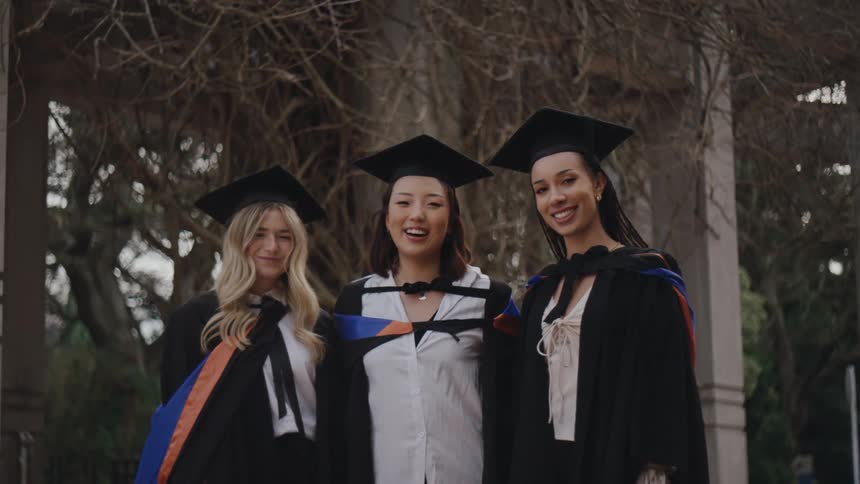 Three women wearing graduation cap and gowns pose outdoors