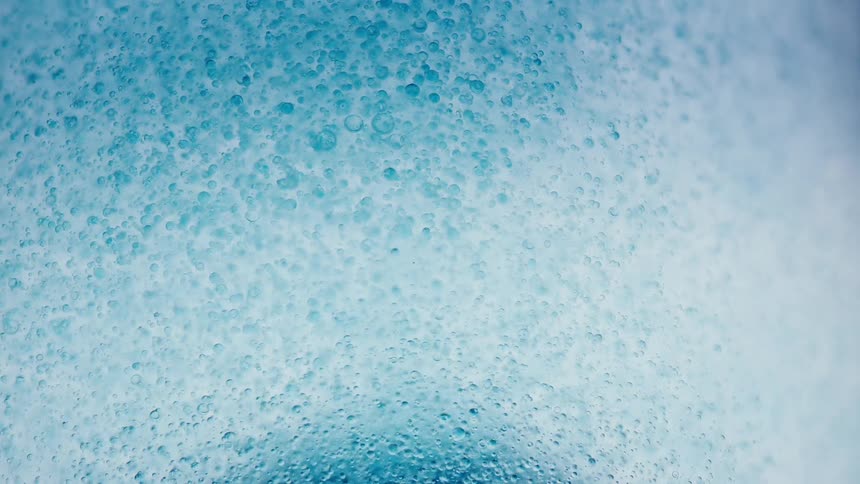 Blue bubbles float through a pale fluid