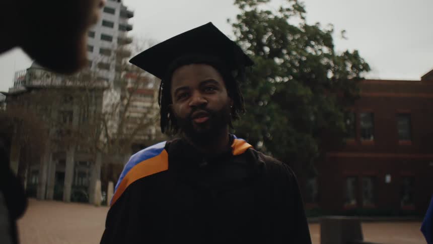 A graduate in cap and gown chats with friends on a city campus