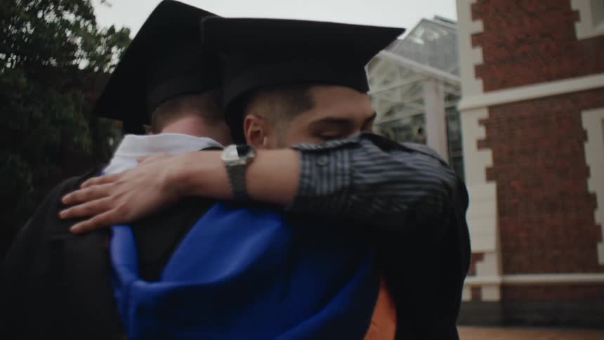 Friends in graduation gowns and caps celebrate by hugging each other
