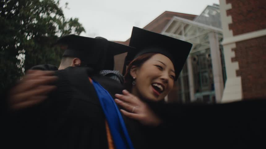 Two graduates hug and talk outside the school
