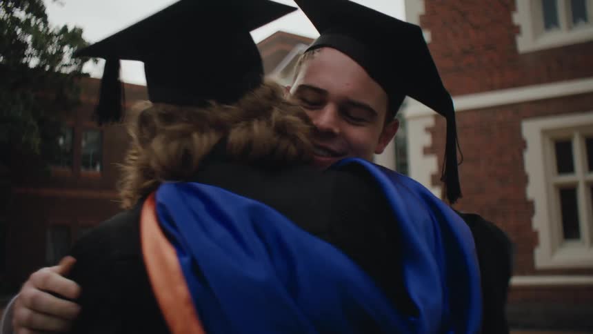 Student friends greeting each other while wearing graduation gowns