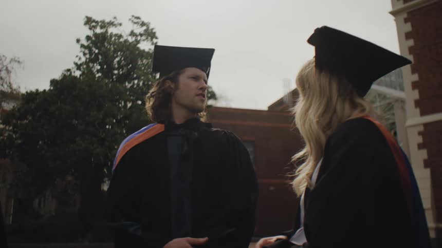 Man and woman talking and both wearing graduation gowns